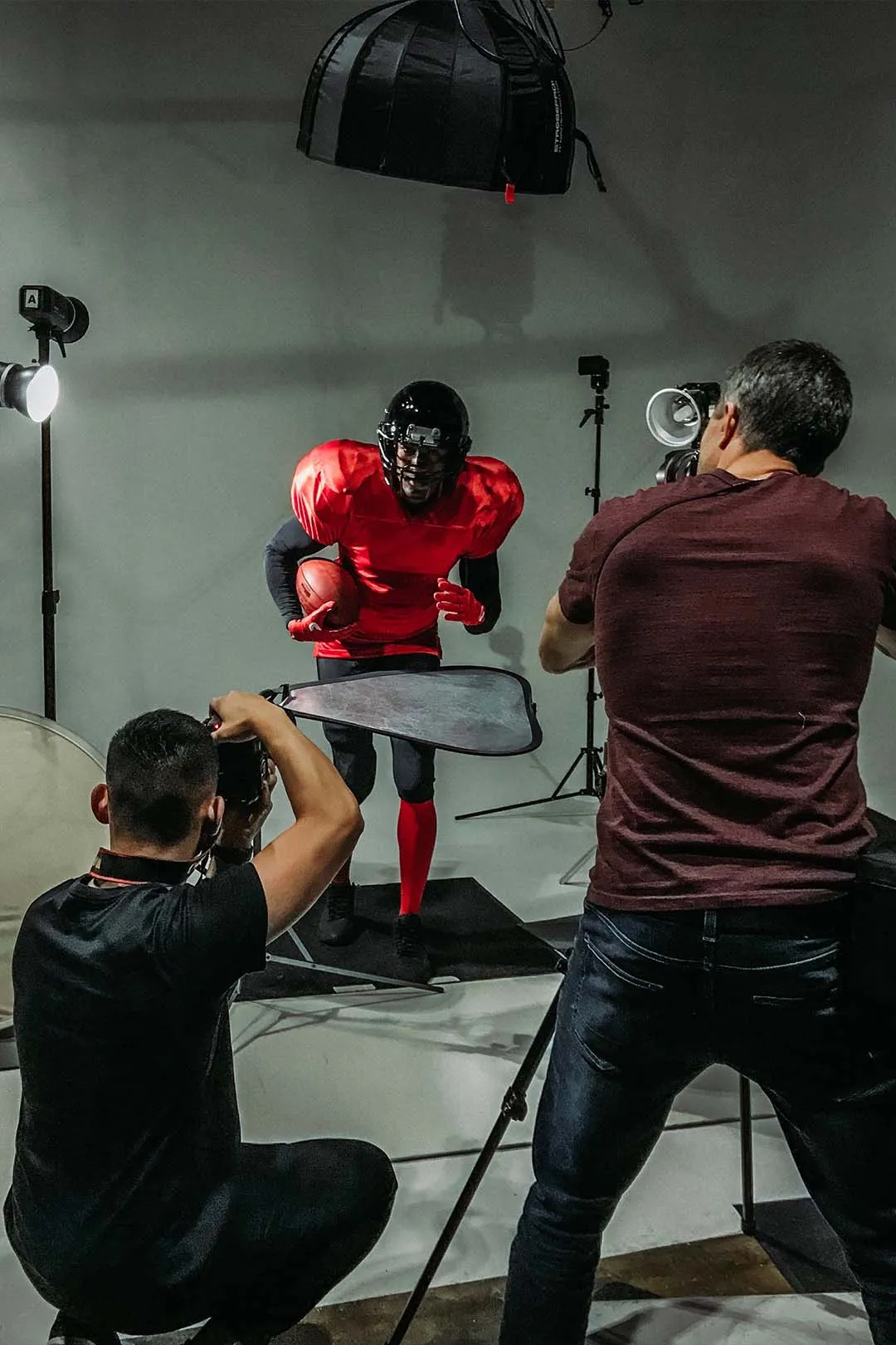 Behind the scenes — a football player being photographed on set with two cameras and a reflector